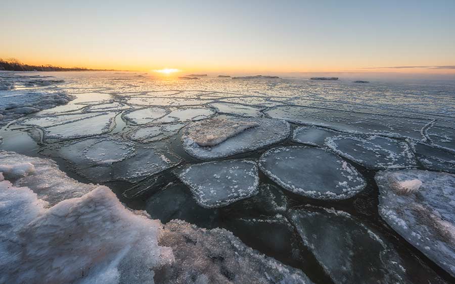 Patches of ice illuminated by a sunrise as seen from the shore.