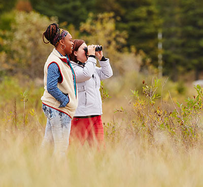 Two women in a field using binoculars.