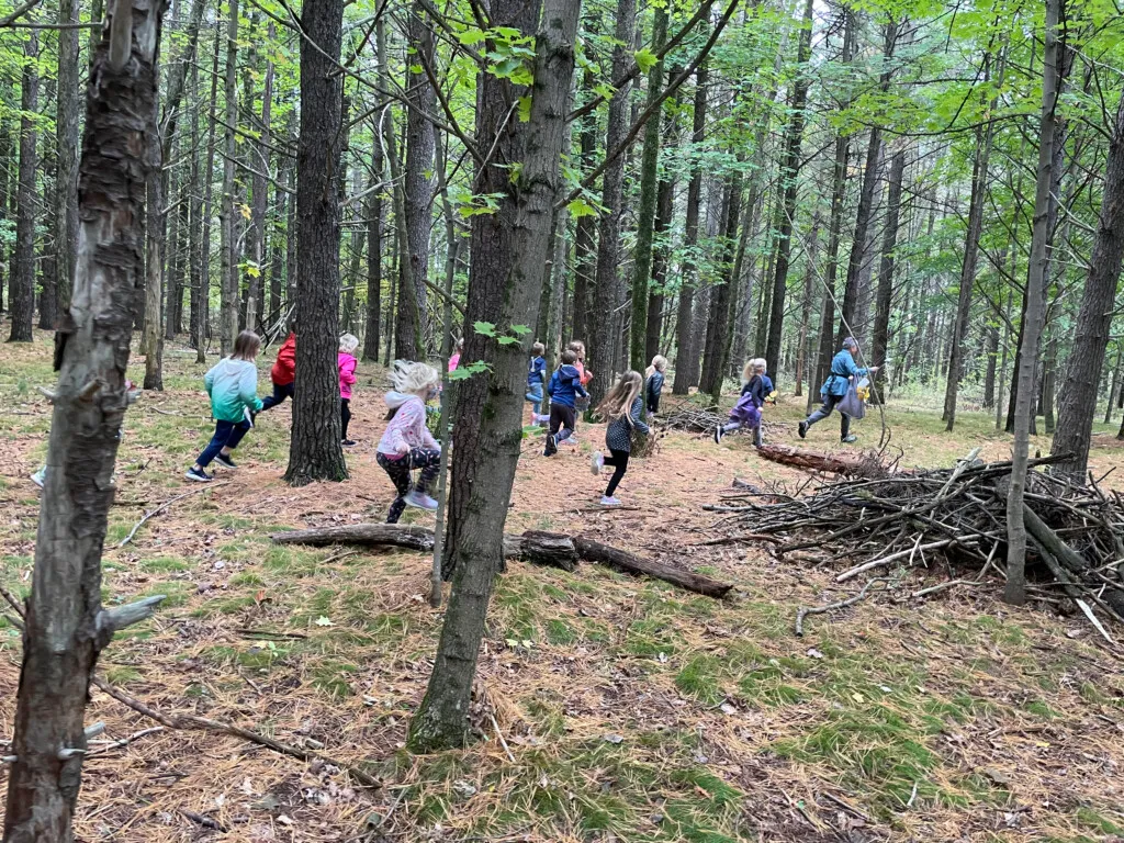 Kids running through the woods with an instructor.