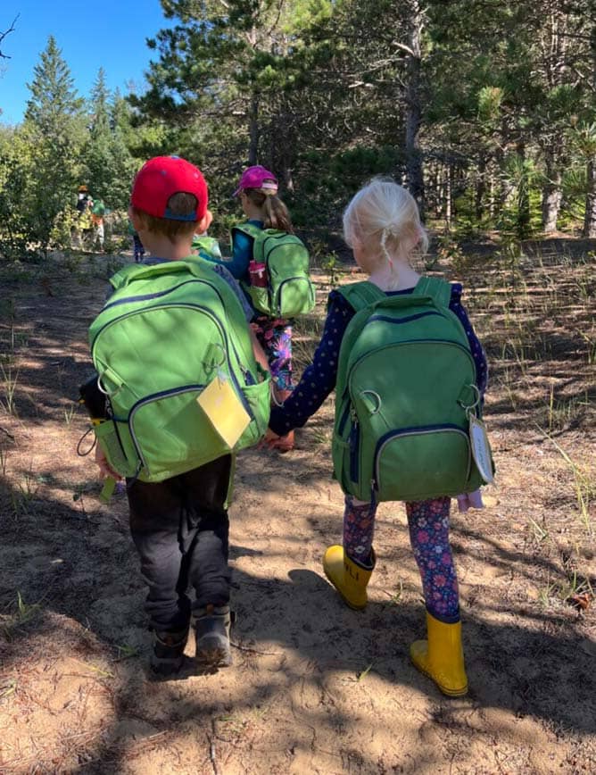 Two campers wearing backpacks holding hands and walking.