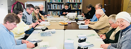 Group of volunteers seated at a table packaging mailing.