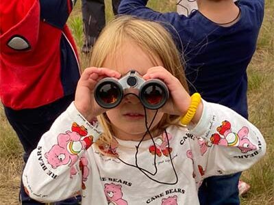 A little girl looking toward the camera through binoculars