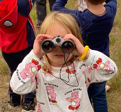 A little girl looking toward the camera through binoculars