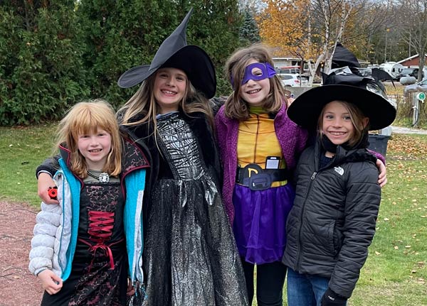 Four young friends arm-in-arm in their Halloween costumes: Two witches, a vampire, and a teenage mutant ninja turtle.