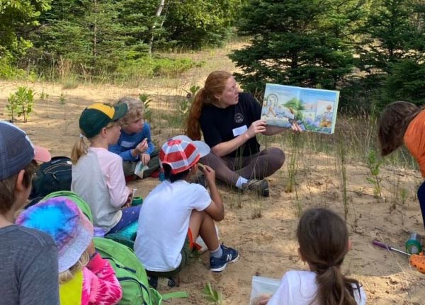 A woman reading a picture book aloud to a group of kids.