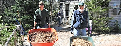 Two men wheeling wheelbarrows full of soil.