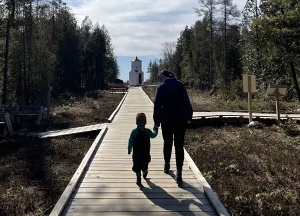 A mom and young son walk down the boardwalk on a sunny day.